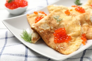 Delicious crepes with red caviar and sour cream on table, closeup