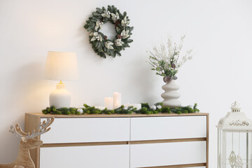Christmas decor and burning candles on cabinet near white wall indoors. Interior design