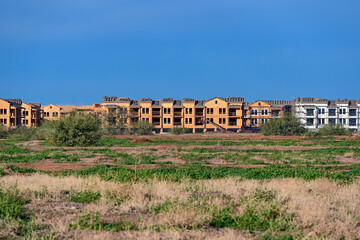 Row of multi story apartment buildings under construction behind an open field, illustrating large scale residential development, framing progress, and expansion of multifamily housing projects