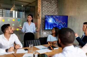 Business professionals from diverse backgrounds engage in discussion about company growth strategies in a contemporary boardroom. They share insights while analyzing data displayed on screens.