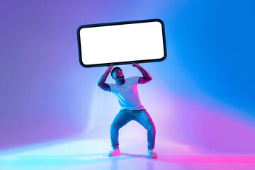 A young man stands with a large blank phone screen held above his head, surrounded by vibrant blue and purple lights. He appears energetic and engaged with his pose.