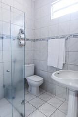 clean functional bathroom interior, white tile with blue accent border, pedestal sink and glass shower, practical small washroom design, bright hygienic toilet and basin, residential apartment rental