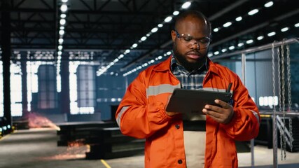 African american engineer at worksite monitoring machinery automation, highlighting steel fabrication, workforce collaboration and industrial activity required in heavy production. Camera B.
