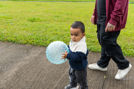 Toddler playing with a spiked translucent ball while walking with his father on a sidewalk in a park - Powered by Adobe