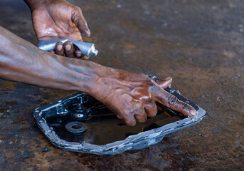 A mechanic's hands apply sealant to a car transmission oil pan for an ATF change. Auto service, vehicle maintenance, transmission repair, and professional garage work concept.