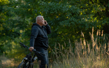 Fototapeta premium An elderly gray-haired man uses a smartphone while cycling through the forest.