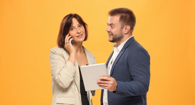 Two professional people with a tablet and a smartphone isolated on a yellow background