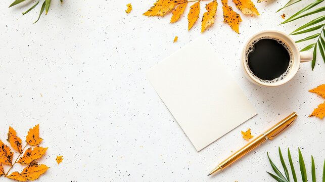 Overhead shot of a coffee cup, blank paper, and pen arranged on a white textured surface, decorated with autumn leaves and greenery.