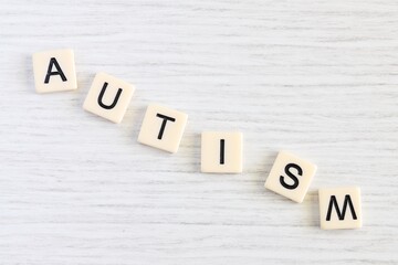 Close up shot of some plastic letter blocks spelling "Autism" in English on white wooden background.