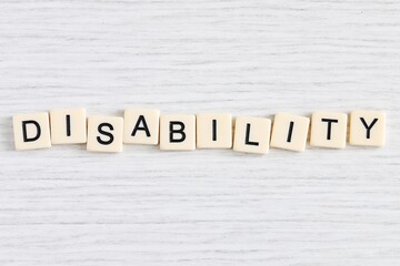 Close up shot of some plastic letter blocks spelling "Disability" in English on white wooden background.