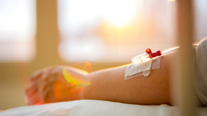 Patient receiving intravenous drip in hospital bed with warm sunlight