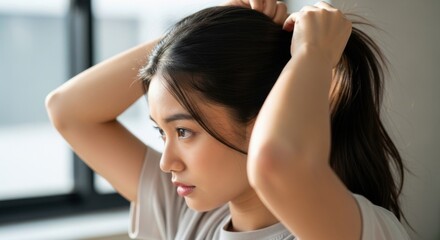 Young woman putting her hair up in a ponytail indoors.