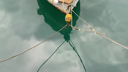 Weathered fishing boat floating on calm turquoise water, ropes and buoys reflected softly below for a tranquil harbor moment