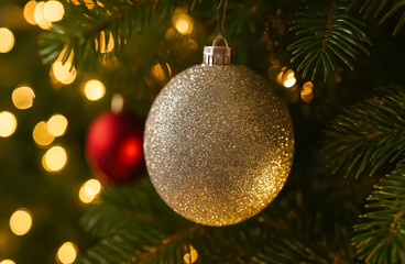 A glittering silver ornament hangs gracefully from a Christmas tree, surrounded by warm festive lights and hints of red.
