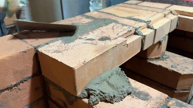 A stove fitter cleans fresh brickwork of excess mortar. He removes it with a trowel. Construction of a heating stove. Close-up.