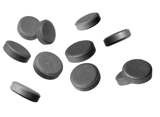 numerous dark grey activated charcoal tablets scattered and isolated against a deep transparent background, highlighting digestive health, internal detoxification, and supplementary medicine.