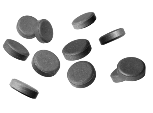 numerous dark grey activated charcoal tablets scattered and isolated against a deep transparent background, highlighting digestive health, internal detoxification, and supplementary medicine.
