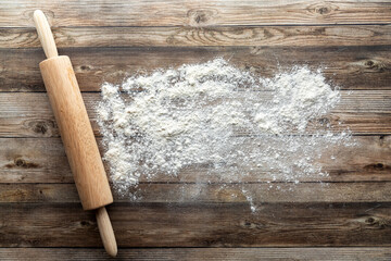 A baking concept background with flour and a rolling pin on a wooden table.