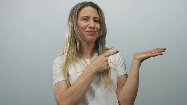 Woman wearing white t shirt finger pointing to palm in grey studio poised for demonstration; invitation.