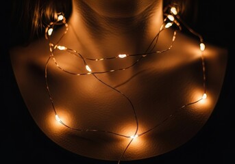 A person's neck and shoulders are adorned with a glowing string of warm fairy lights against a dark background.