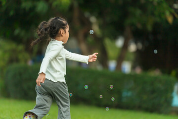 happy toddler girl running and playing soap bubble in park
