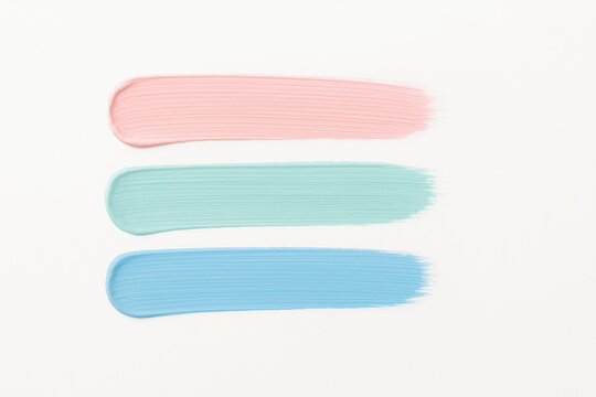 Flat lay three parallel painter brush strokes in soft pastel tones pink mint and sky blue neatly aligned on bright white background