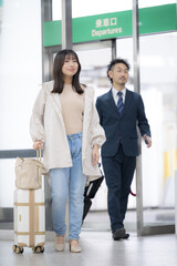 駅や空港のような場所でスーツケースを持って移動する女性　旅行や遊びに行くイメージ全身