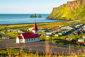 View of basalt stacks Reynisdrangar, black sand beach, church and city of Vik, Iceland