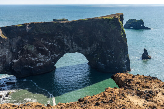 Dyrholaey coast cliffs and rocky arch, Vik, South Iceland. Reynisfjara ocean black volcanic sand beach in far. - Powered by Adobe