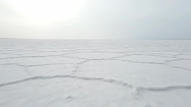 Cinematic drone shot sweeping slowly over an infinite white desert salt flat meeting a hazy blank horizon line under diffuse light blank horizon line, surreal landscape, conceptual