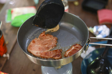 Satisfying meal of juicy pork steak cooking in frying pan on portable camping stove. Relaxing outdoor food preparation during an adventure trip represents simple lifestyle