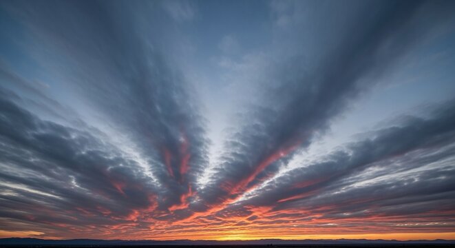 Dramatic sunset sky with radiating clouds painted in vibrant orange and red hues against a deep blue twilight, creating a breathtaking natural spectacle