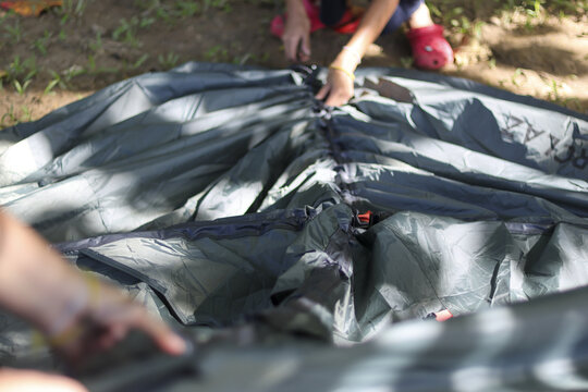 Focused child and adult cooperate on an outdoor adventure, setting up camping tent together. Teamwork activity on sunny day helps assemble shelter for holiday