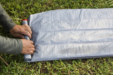 Focused man rolling up grey air mattress on grass. Careful preparation for packing up camping gear...