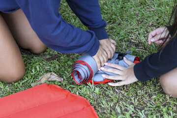 Two young people outdoor on green grass, focused on activity of rolling sleeping pad. An image of...
