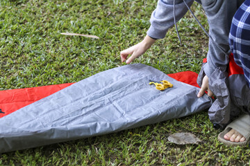 Focused person preparing gray air mattress on green grass for outdoor camping adventure. Setting up...