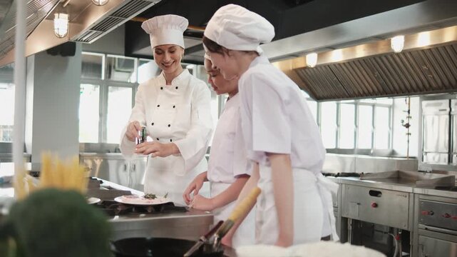 Female chef demonstrates to intern student girls, cooking class in catering restaurant kitchen, professional gourmet master in delicious cuisine, ingredients preparation in eatery, and culinary meals.