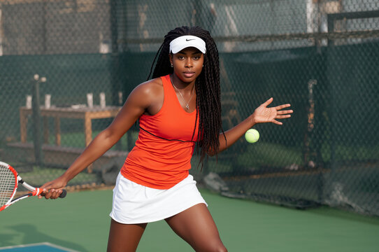 Focused and determined young african american female tennis player in an orange top hitting a forehand shot on an outdoor court, symbolizing professional sport, fitness, and competitive action.