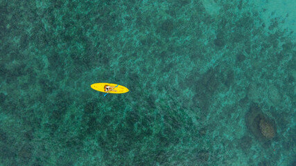 Aerial view woman bright yellow kayak with in the vast expanse of crystal clear turquoise water. The seabeds rocky texture is visible beneath the surface, concept marine environment	