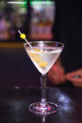 A classy cocktail with a olive garnishing in a bar setting