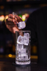 A bartender is carefully putting ice into a glass