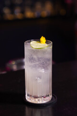 Elegant cocktail in a tall glass, garnished with lime and flower, set on a dark surface, inviting relaxation and enjoyment