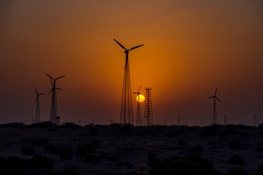 The setting sun with windmills silhouetted against an orange sky at Jaisalmer India. - Powered by Adobe