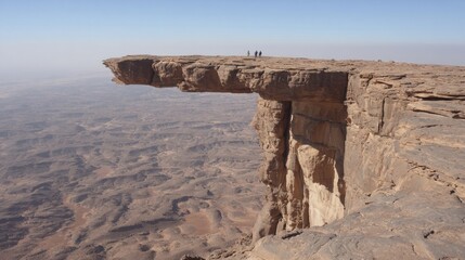 A rugged landscape featuring a rock formation with a sheer drop and a few people at the edge