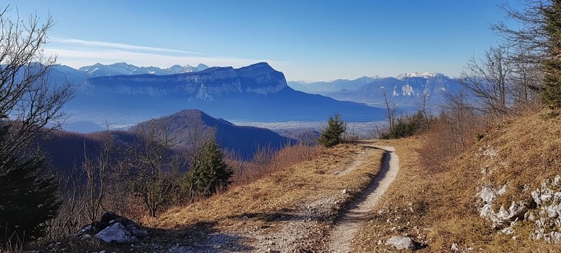 Mountain trail winds through a landscape of hills and distant peaks under a clear blue sky - Powered by Adobe