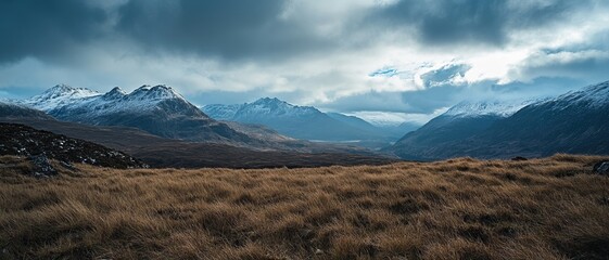 Panoramic view of snow-capped mountains under a dramatic sky over a field of dry grass