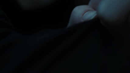 Close-up of fingertips gently brushing a dark fabric in dim, moody lighting, highlighting subtle texture and quiet tactile motion between skin and cloth across macro frames - Powered by Adobe