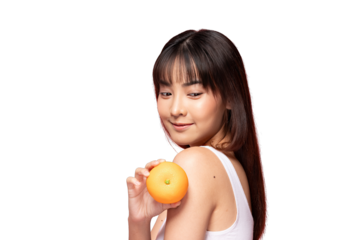 Asian Young woman holding orange near shoulder with gentle smile and soft studio lighting conveying fresh healthy mood