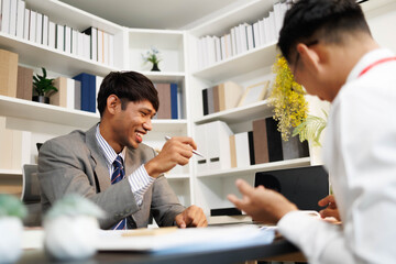 Two men are sitting at a desk, one of them is holding a piece of paper. They are having a conversation, and it seems like they are discussing something important. The atmosphere is tense
