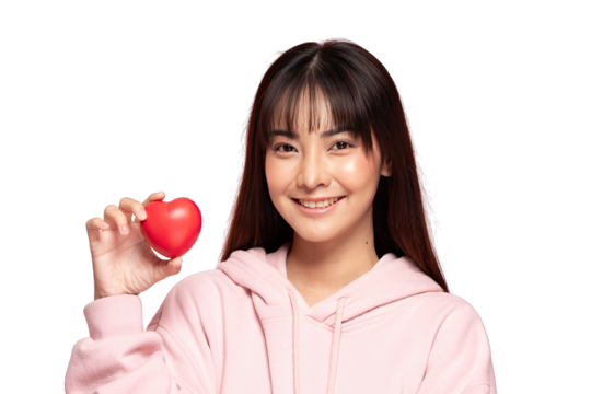 Asian Young Asian woman holding red heart stress ball smiling in pink hoodie conveying warmth and care, healthcare concept and positive emotion - Powered by Adobe